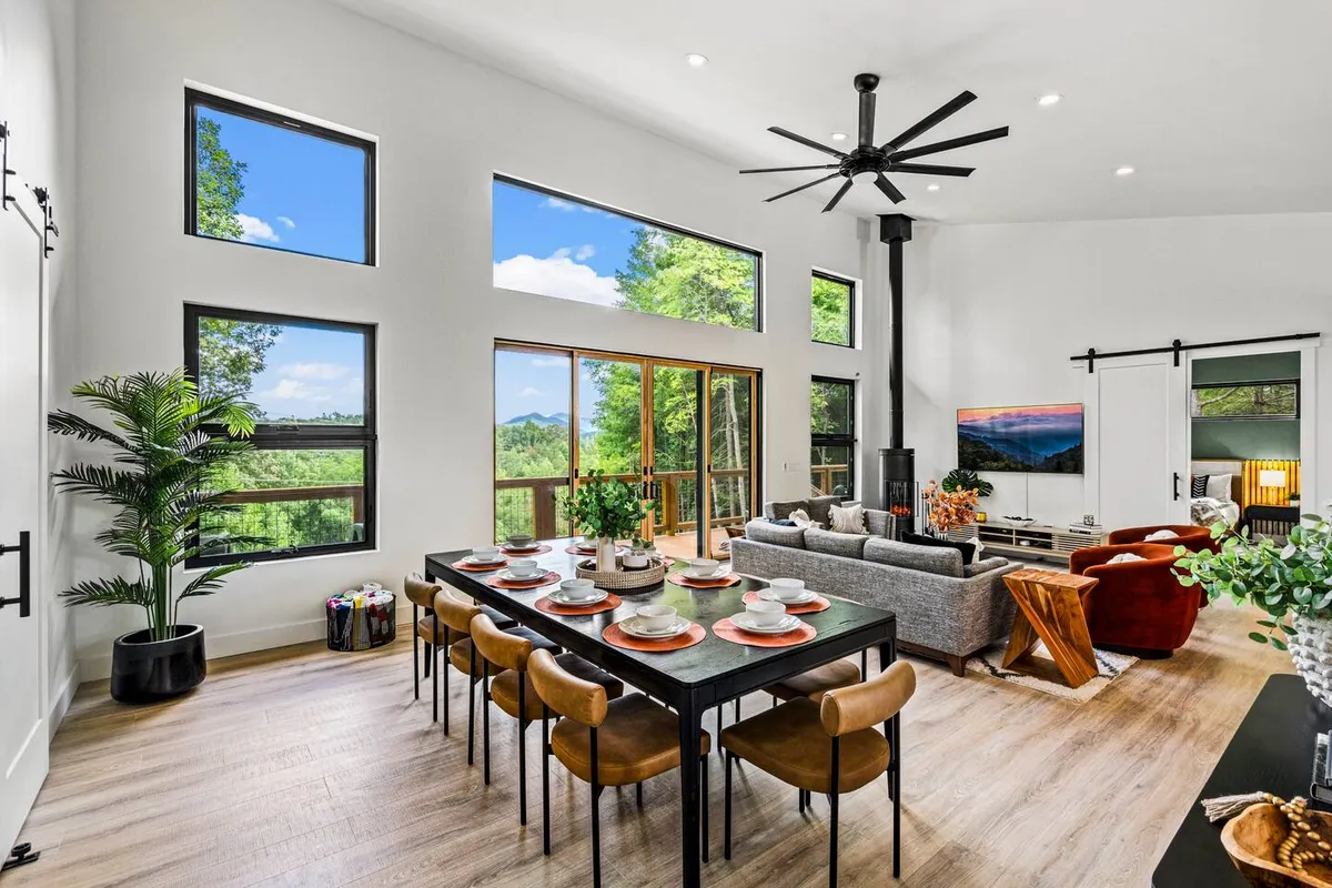 A stylish dining area set for a meal, with a large table and comfortable chairs. Floor-to-ceiling windows offer panoramic views, merging the interior with the outdoors, and a cozy seating area is nearby for after-dinner relaxation.