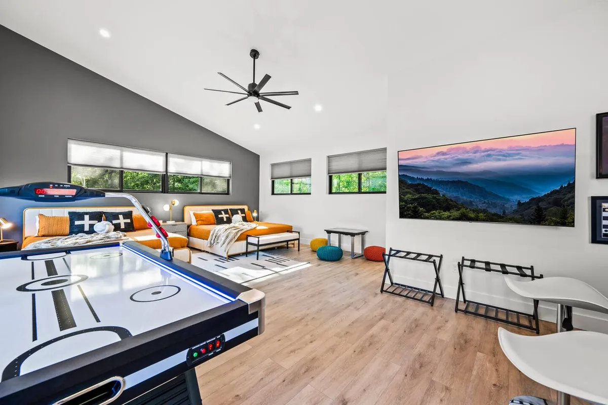 Inside, a lively game room features an air hockey table, bright orange sofas, and artwork depicting mountain landscapes. The space is designed for family fun and relaxation after a day of outdoor activities.