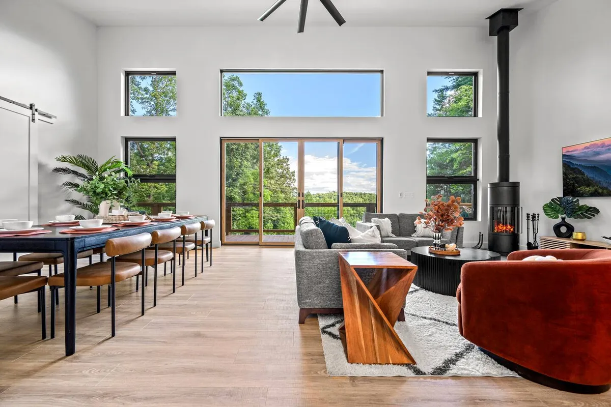 A warm dining space with a large table, plush seating area, and floor-to-ceiling windows that flood the room with light. A wood-burning stove adds a cozy touch, perfect for evening gatherings or festive dinners.