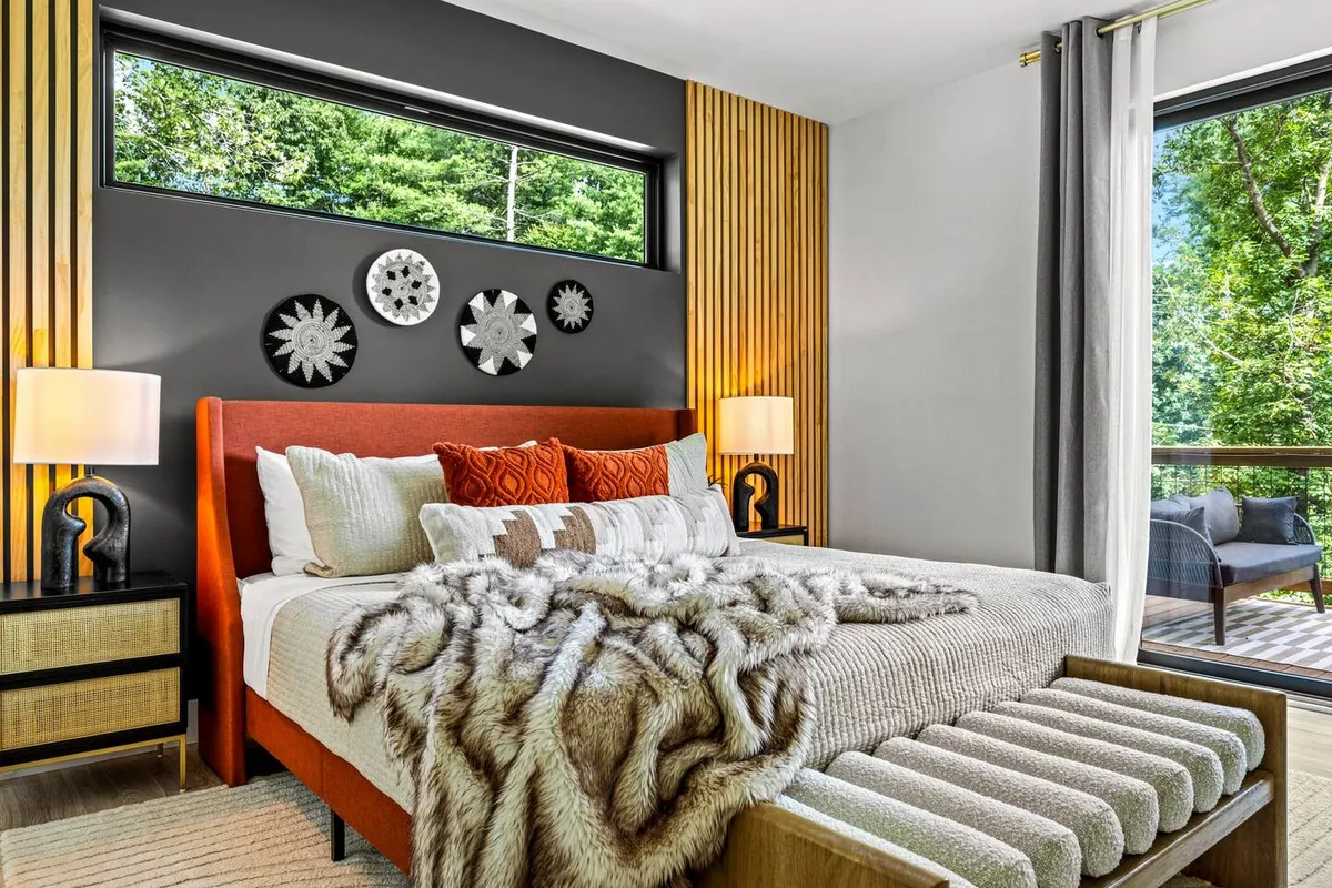A cozy bedroom with a soft bed, decorative wall art, bedside lamps, a textured throw blanket, and a window that lets in natural light and reveals a scenic view. The room radiates tranquility and warmth, ideal for restful sleep and relaxed mornings.