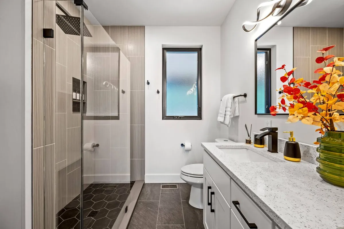 A modern, spa-inspired bathroom featuring a glass shower enclosure, sleek sink, and decorative plant. The overall vibe is refreshing and serene, ideal for relaxing and self-care rituals after a long day.